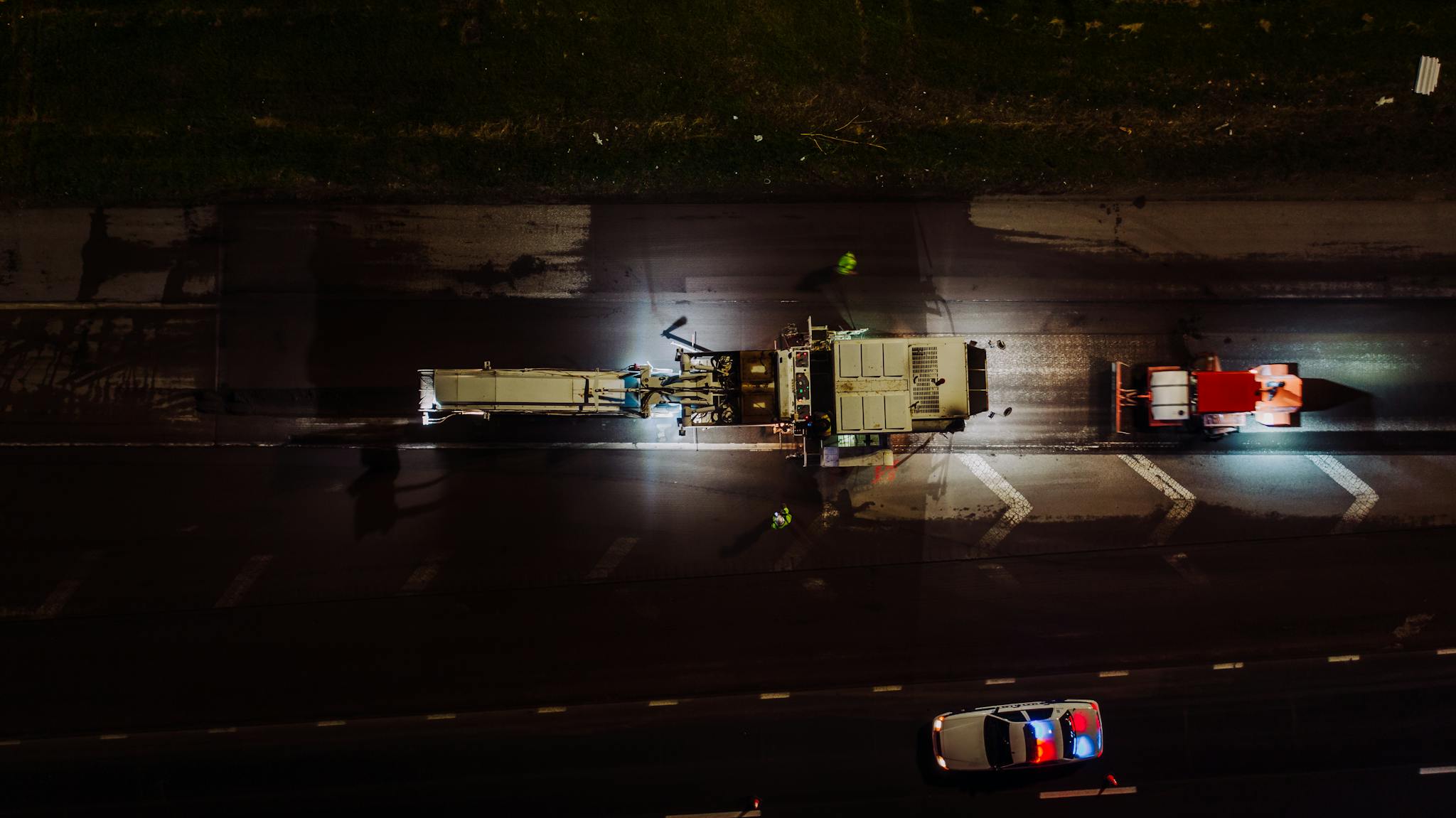 Top view of specialized vehicles with lights on repairing road and laying asphalt and concrete at night